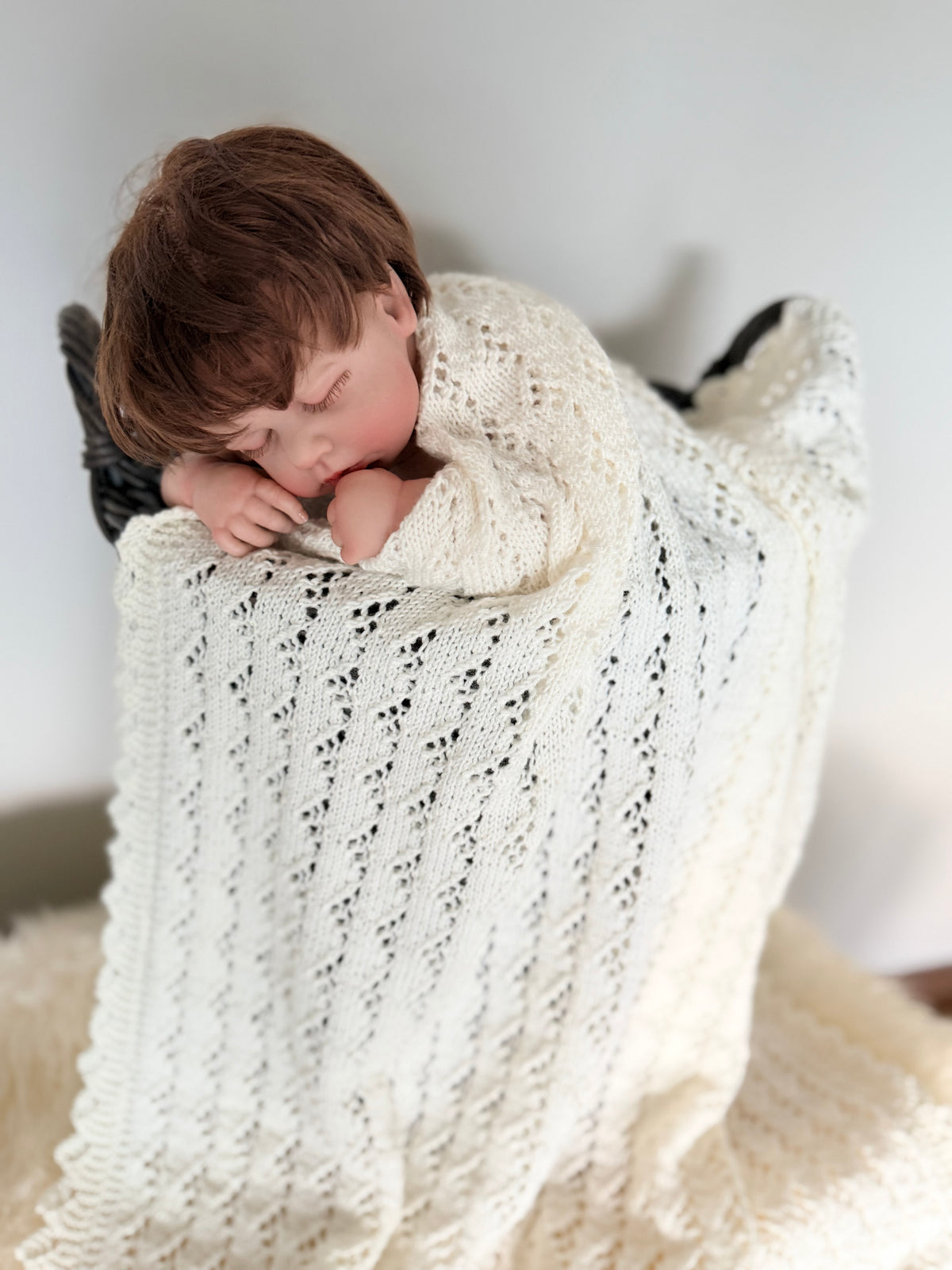 Sovende baby pakket inn i et hvitt strikket teppe fra Mønsteridyll